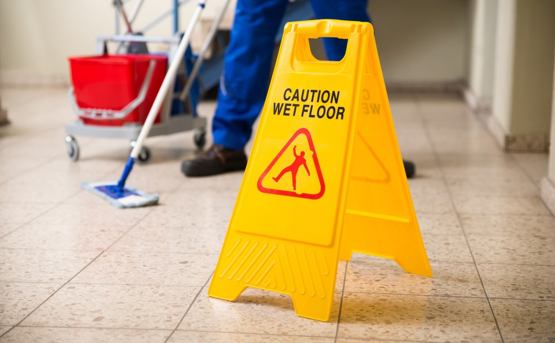 A bright yellow wet floor sign standing as a worker mops the floor behind 