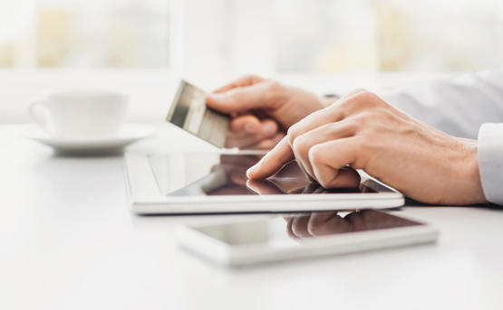 a pair of hands hold a debit card whilst tapping numbers into a tablet