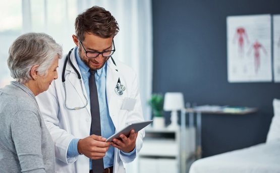 A medical professional talks to a patient whilst looking at a tablet 