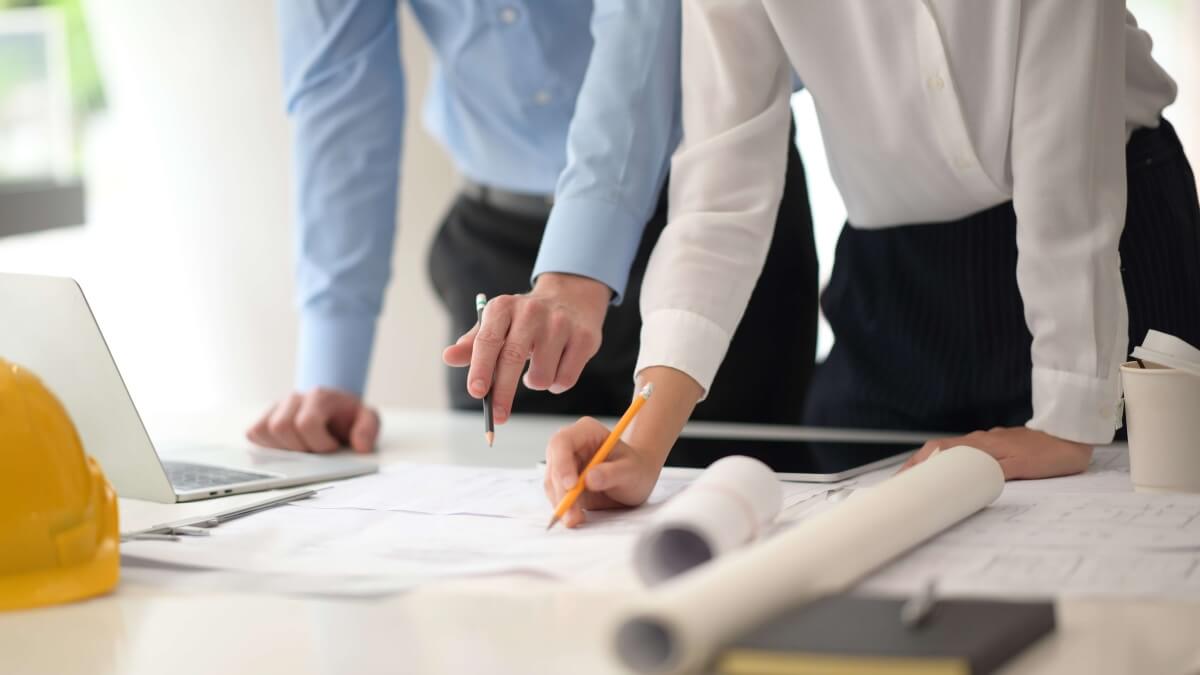 Stock image of man and a woman looking a building plans on a desk